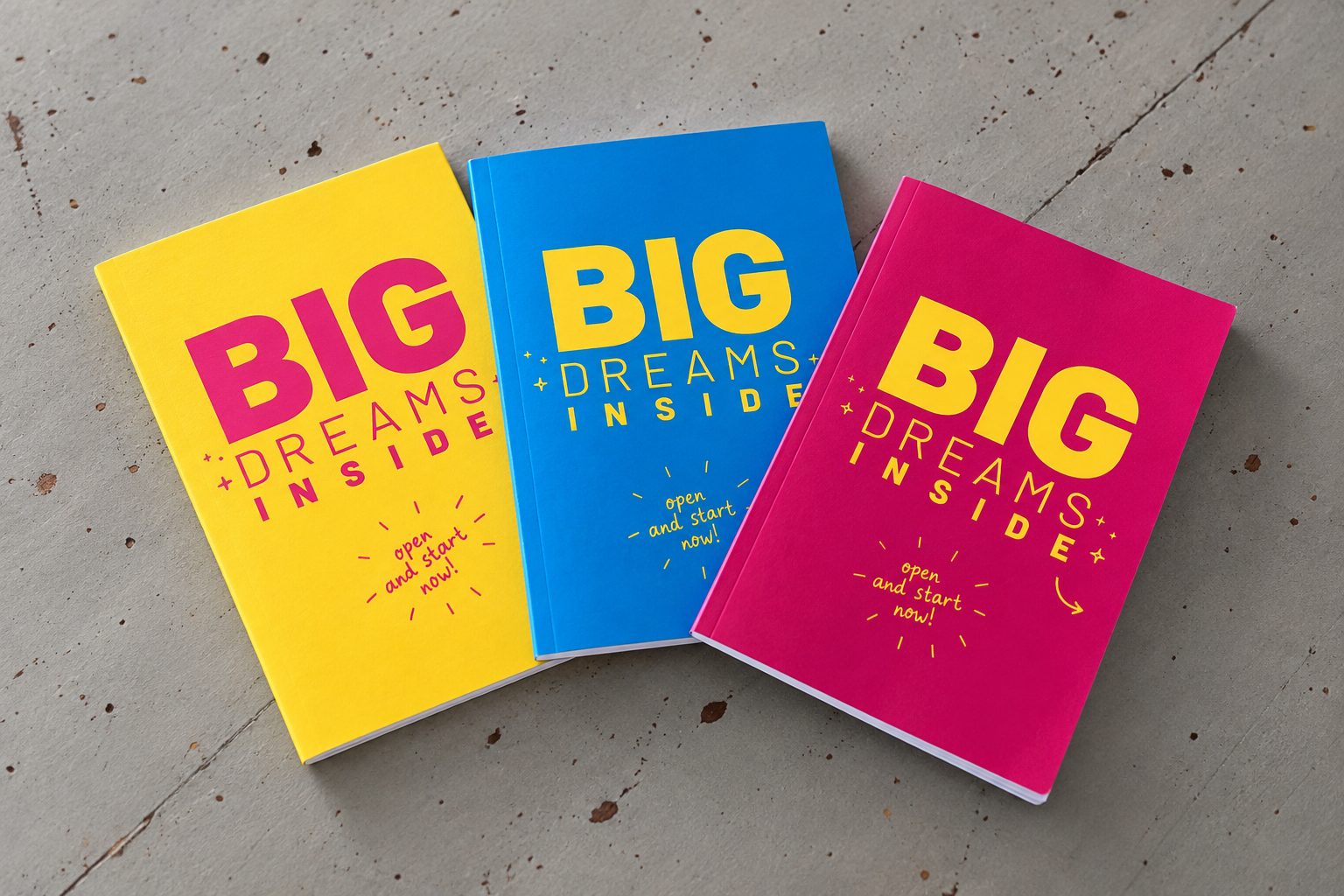 Três cadernos Big Dreams Inside, amarelo, azul e magenta, sobre betão