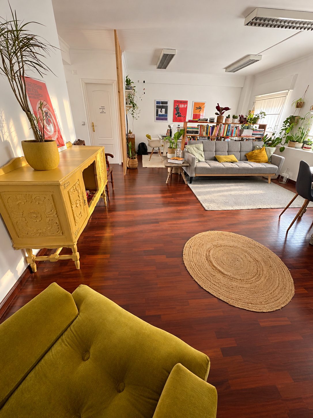 Entrada do estúdio, com o sofá verde, o móvel amarelo e a zona de estar ao fundo