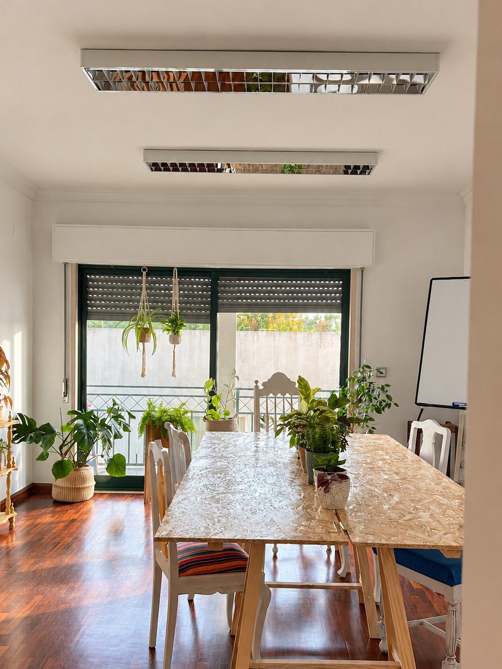 Mesa comprida de trabalho junto à janela, com cadeiras de assentos coloridos